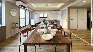 A modern kitchen with a long wooden table set for dining, equipped with plates, glasses, and a vase of flowers. - M's Lea Building (Hiroshima)