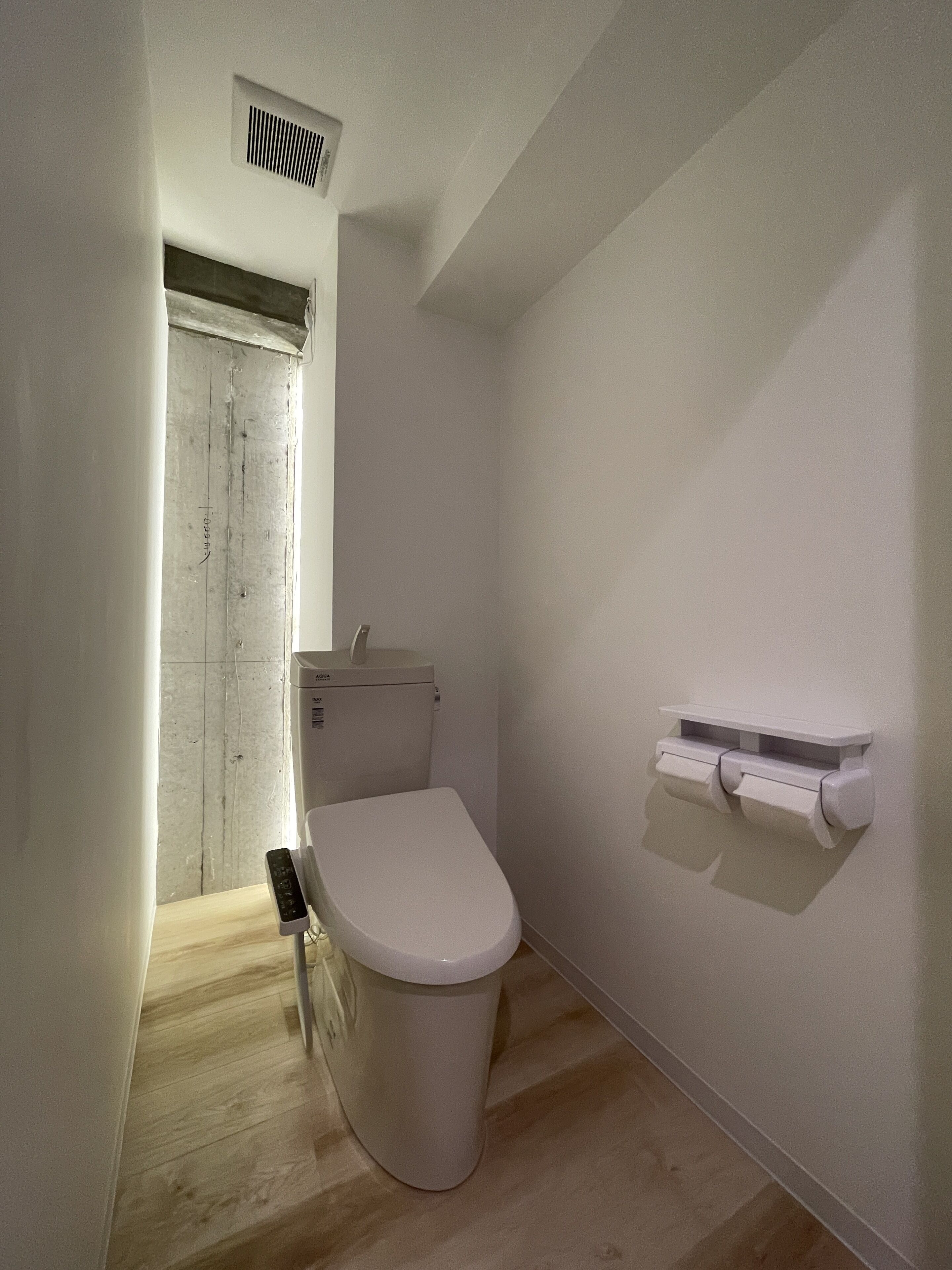 A small, narrow bathroom with a toilet, a hand dryer, and a toilet paper holder on the wall.