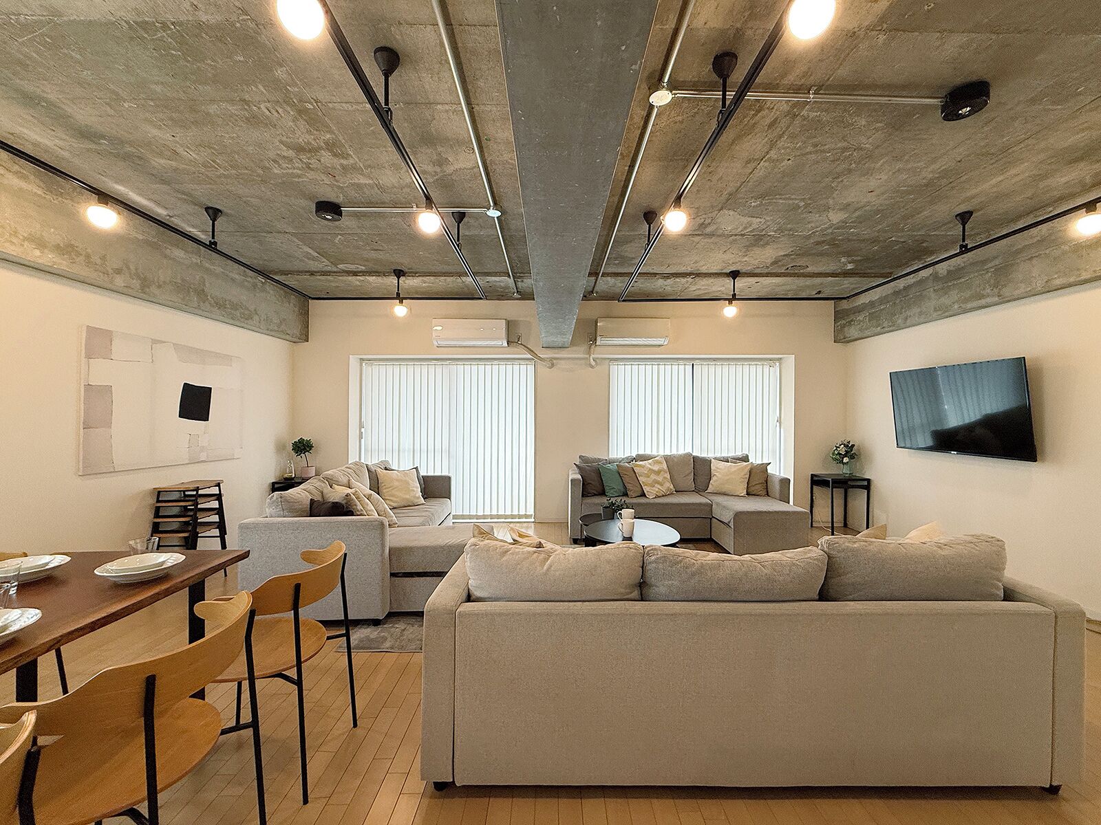 A modern living room with a sofa, a dining table with chairs, and a TV mounted on the wall.