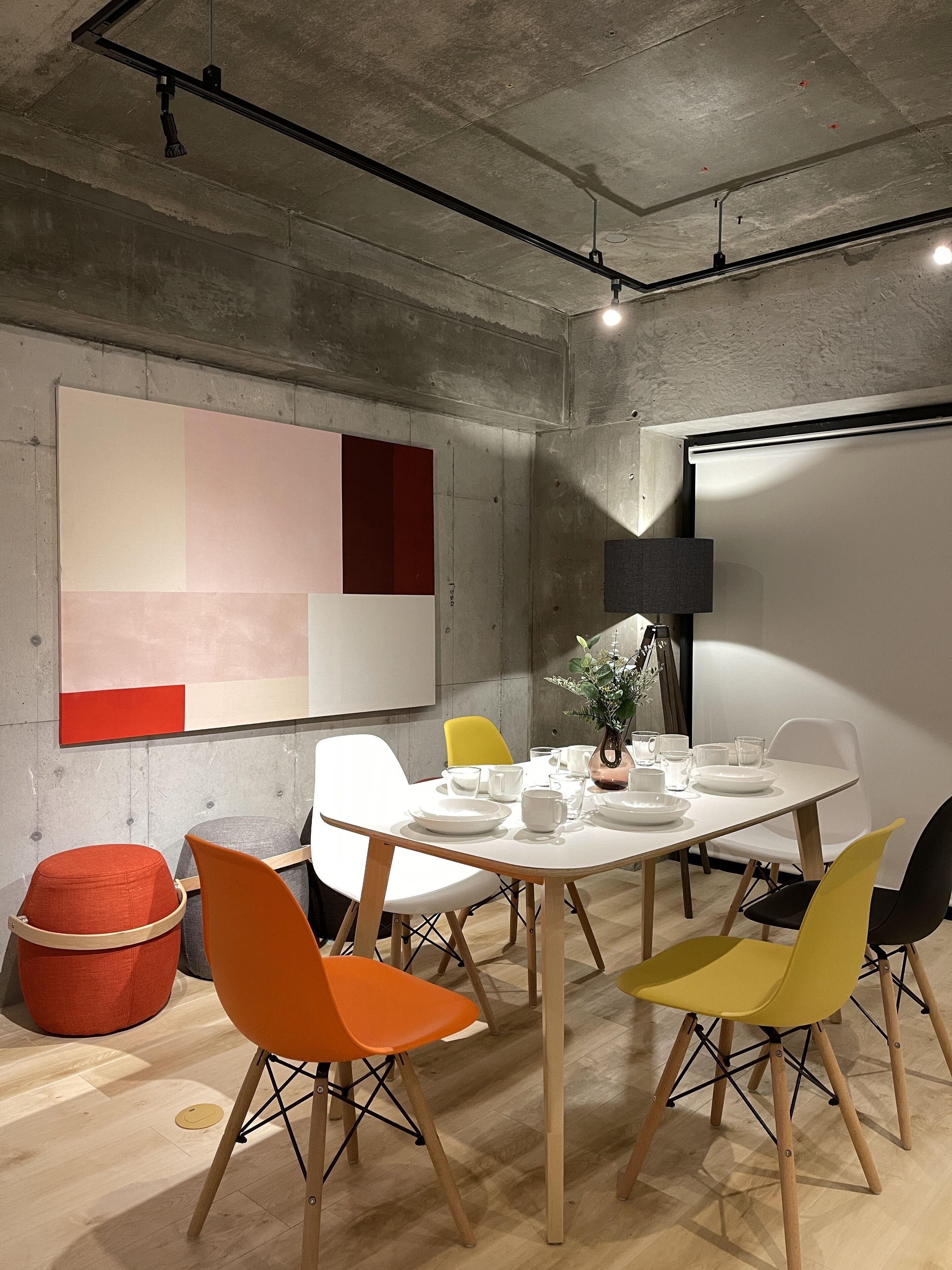 A modern meeting room with a white table, colorful chairs, a large abstract painting, and a projector screen.