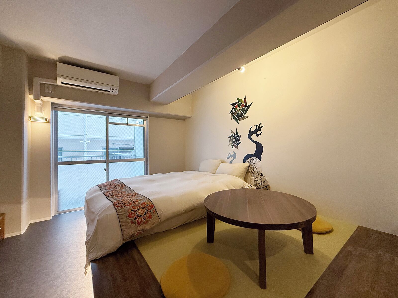 A bedroom with a bed, a round table, and a wall-mounted air conditioner.