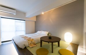 Un dormitorio moderno con una cama, una mesa redonda de madera y una lámpara de pie.