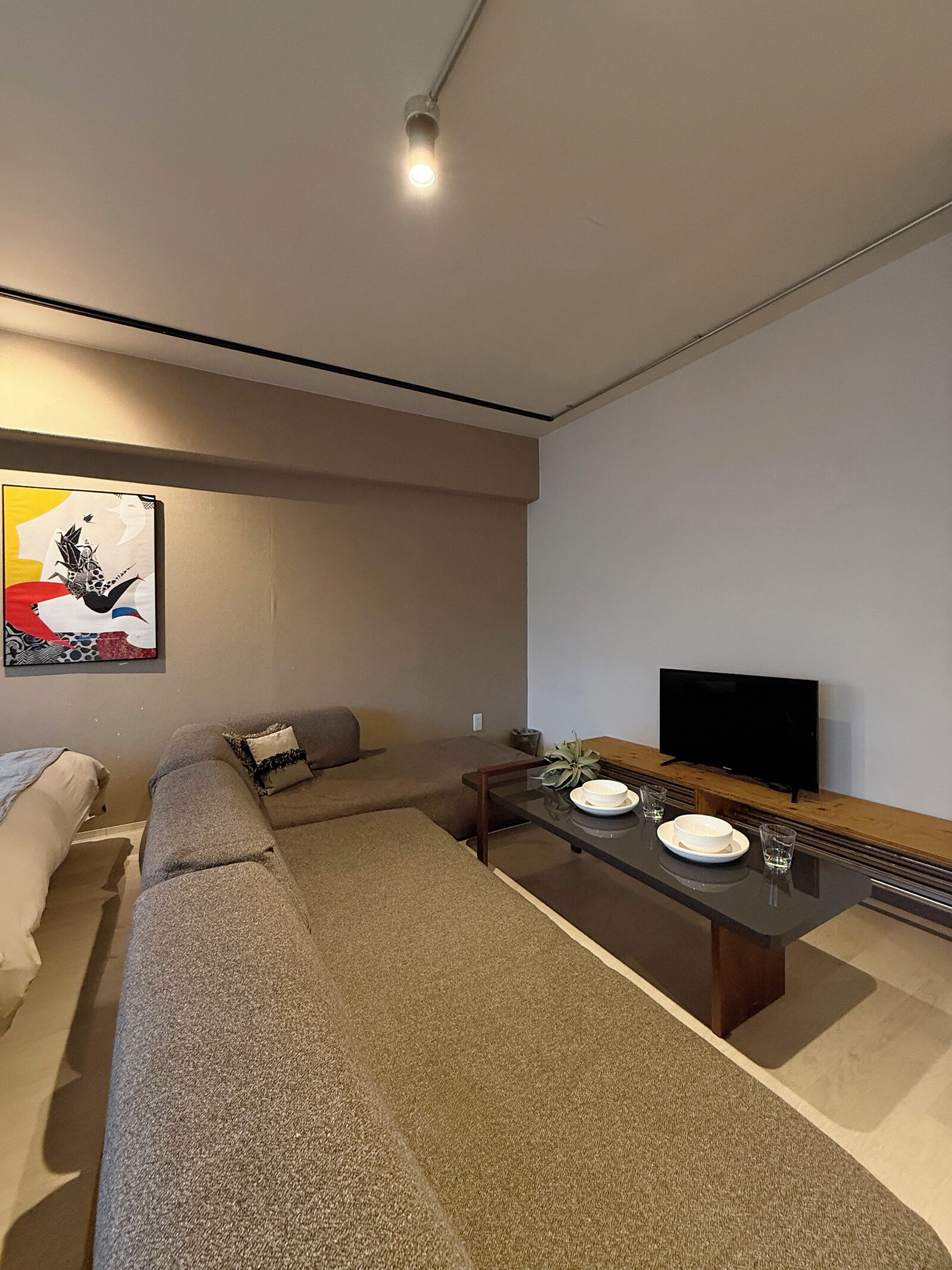 Ein modernes Wohnzimmer mit einem Ecksofa, einem Flachbildfernseher, einem Esstisch mit Tellern und Gläsern sowie einem Wandbild.