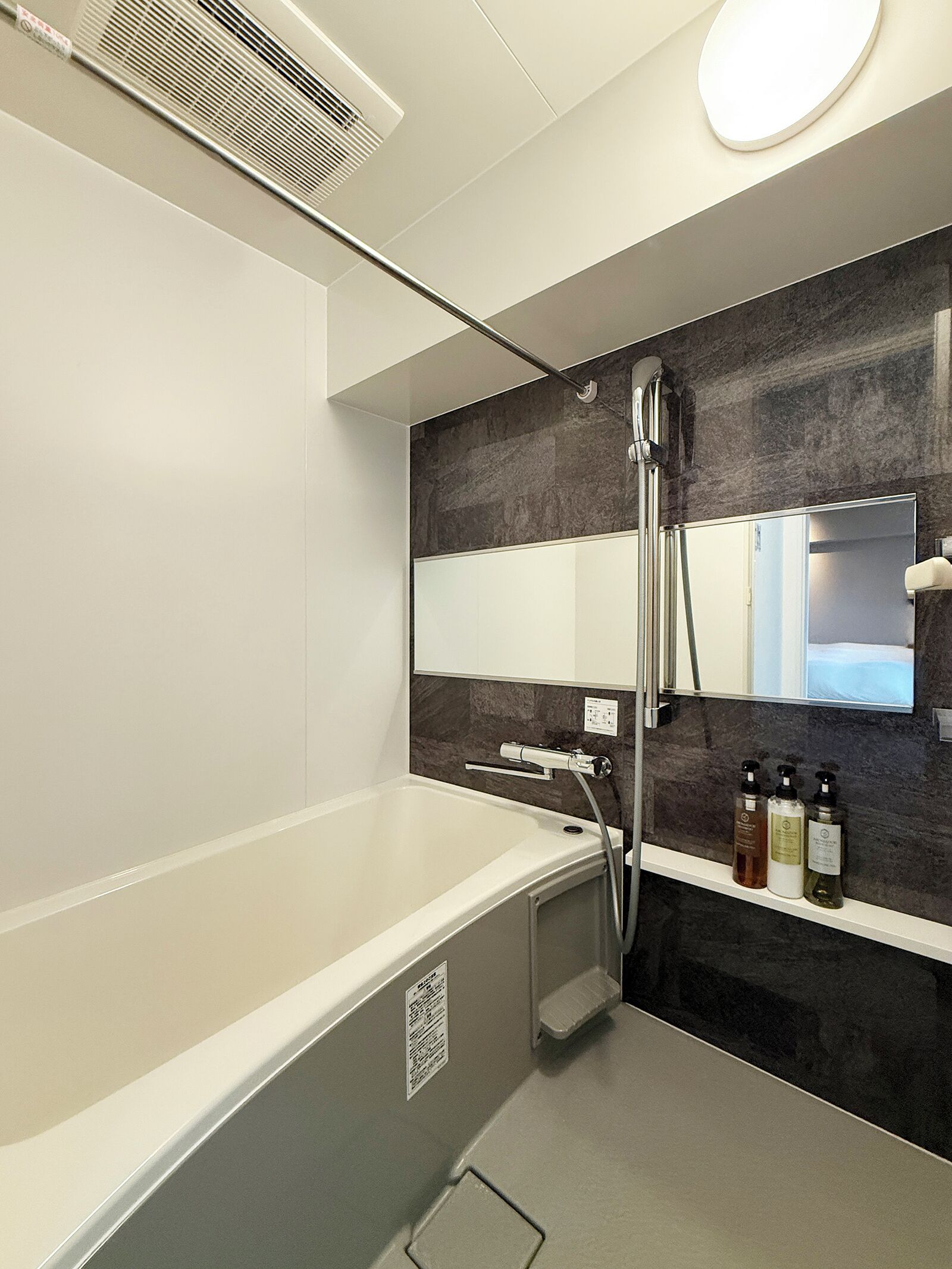 A modern bathroom with a bathtub, a shower, a mirror, and a shelf with toiletries.