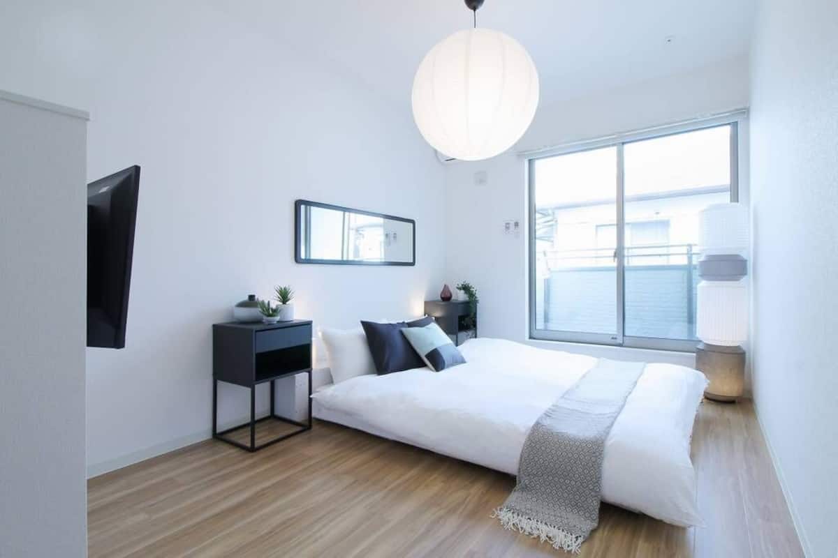A modern bedroom with a large bed, a bedside table, a mirror, and a window with a view of the city.