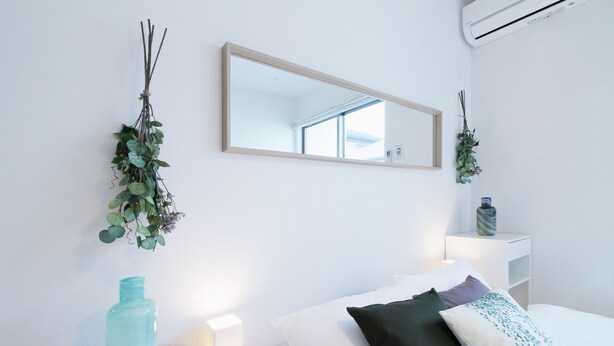 Een minimalistische slaapkamer met een bed, nachtkastje en spiegel.