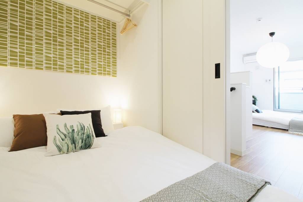 Une chambre d’hôtel moderne avec un grand lit, une fenêtre avec des stores, une lampe de chevet et une vue sur la chambre voisine.