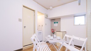 Een kamer met een witte tafel gedekt voor vier personen, witte stoelen, een raam en een deur.