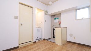 Een gang met een houten vloer, een deur, een wasmachine en een raam.