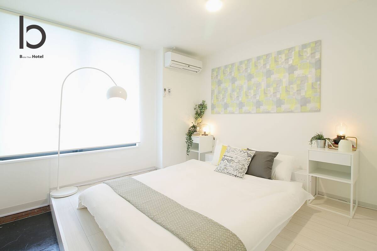 A modern hotel room with a large bed, a desk, a standing lamp, and a wall-mounted air conditioner.