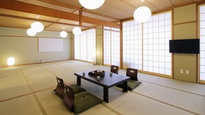 A traditional Japanese room with tatami flooring, a low table with cushions, and sliding shoji doors. - Hanagin Building (Hiroshima)