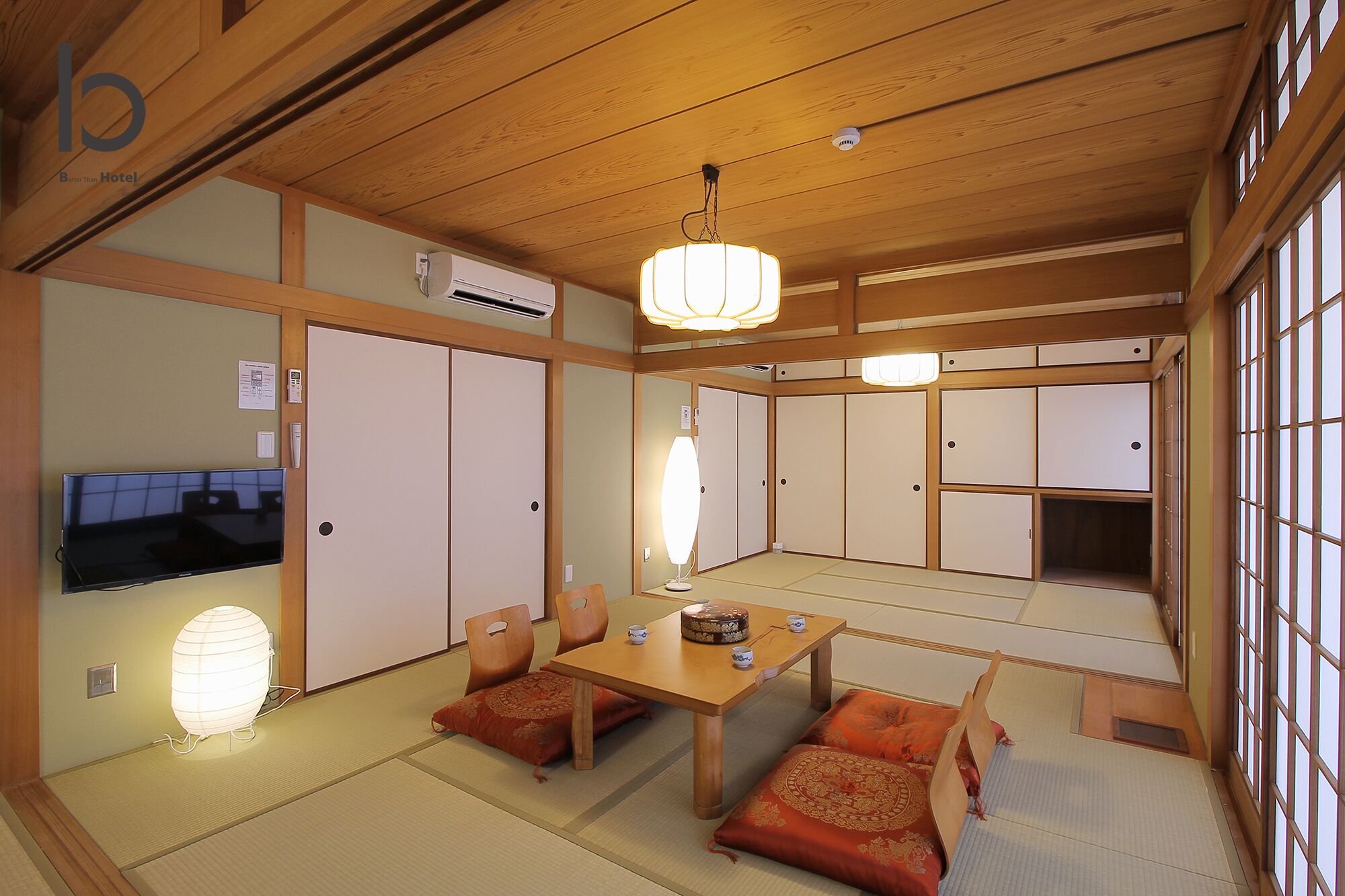 A traditional Japanese-style room with tatami flooring, sliding shoji doors, a wooden ceiling, and a television.