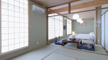Una habitación tradicional japonesa con suelo de tatami, una cama con almohadas, una pequeña mesa con tazas y un ventanal con persianas de celosía.