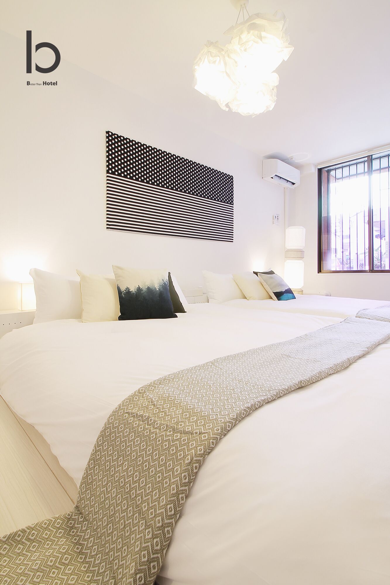 Quarto de hotel com uma cama grande, manta estampada, obra de arte na parede e janela com persianas.