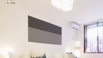 Quarto de hotel com uma cama grande, manta estampada, obra de arte na parede e janela com persianas.