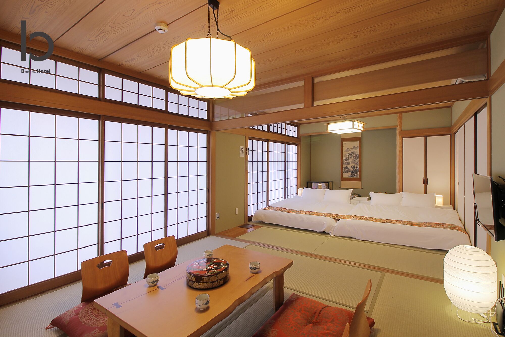A traditional Japanese-style room with tatami flooring, a low wooden ceiling, and sliding shoji doors. There is a bed with white bedding, a table with a tea set, and a hanging lantern.