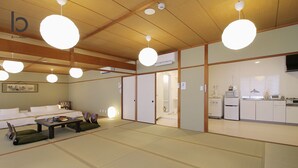 A traditional Japanese-style room with tatami flooring, a low table with cushions, and a sliding door leading to a kitchen area with modern appliances. - Hanagin Building (Hiroshima)