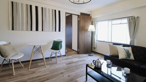 Ein modernes Wohnzimmer mit einer Couch, einem Couchtisch und zwei Sesseln. Ein großes Fenster mit Vorhängen, eine Tür und eine Wand mit vertikalen Streifen sind zu sehen.