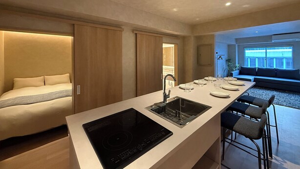 A modern kitchen with an island, built-in oven, and a dining area with a sofa and bar stools. - Ishiki Building (Hiroshima)