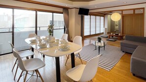 A modern living room with a dining area, featuring a wooden ceiling, large windows, and a grey sofa. - Mbuilding (Hiroshima)