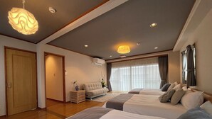 A hotel room with two beds, a sofa, a small side table, and a large window with curtains. - Mbuilding (Hiroshima)