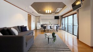 A modern living room with a sofa, a dining table with chairs, a kitchen area, and a large window with a view. - Mbuilding (Hiroshima)