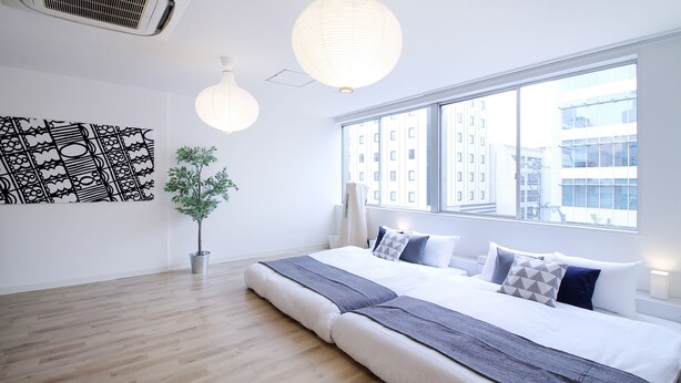 A modern hotel room with a large bed, a potted plant, and a view of buildings through the window.