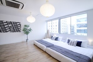 A modern hotel room with a large bed, a potted plant, and a view of buildings through the window. -  Nikke Building (401, 402) (Hiroshima)