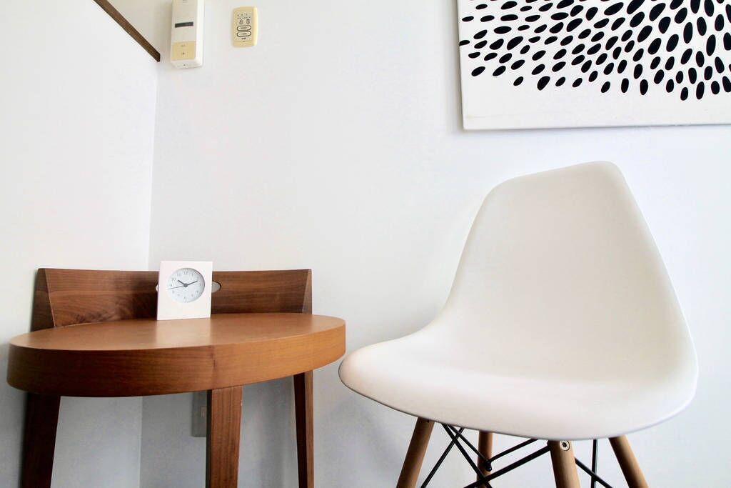 A round wooden table with a white clock and a white chair with a geometric design.