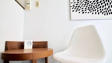 A round wooden table with a white clock and a white chair with a geometric design.