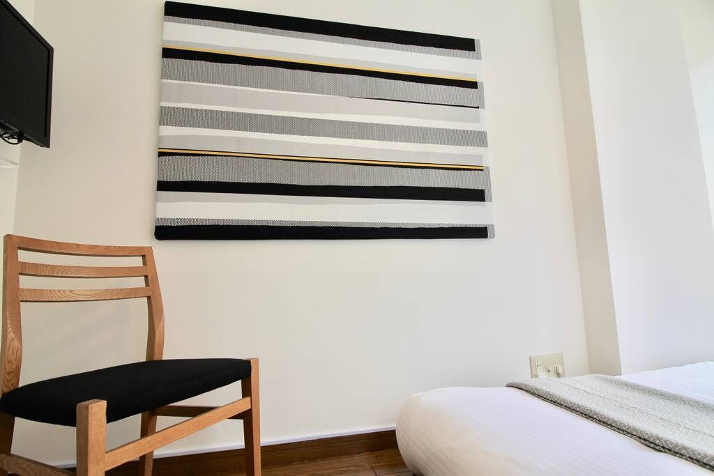 Una habitación con una cama, una silla de madera y una obra de arte en la pared.