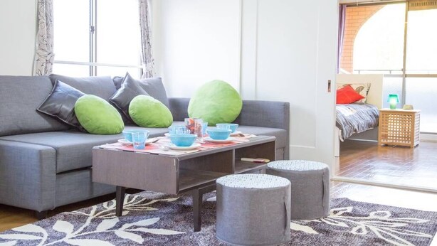 Una sala de estar moderna con un sofá gris, cojines verdes, una mesa de centro con cuencos azules y otomanas grises.
