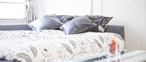 A bed with a floral-patterned bedspread, a gray sofa, and a small table with a glass container.