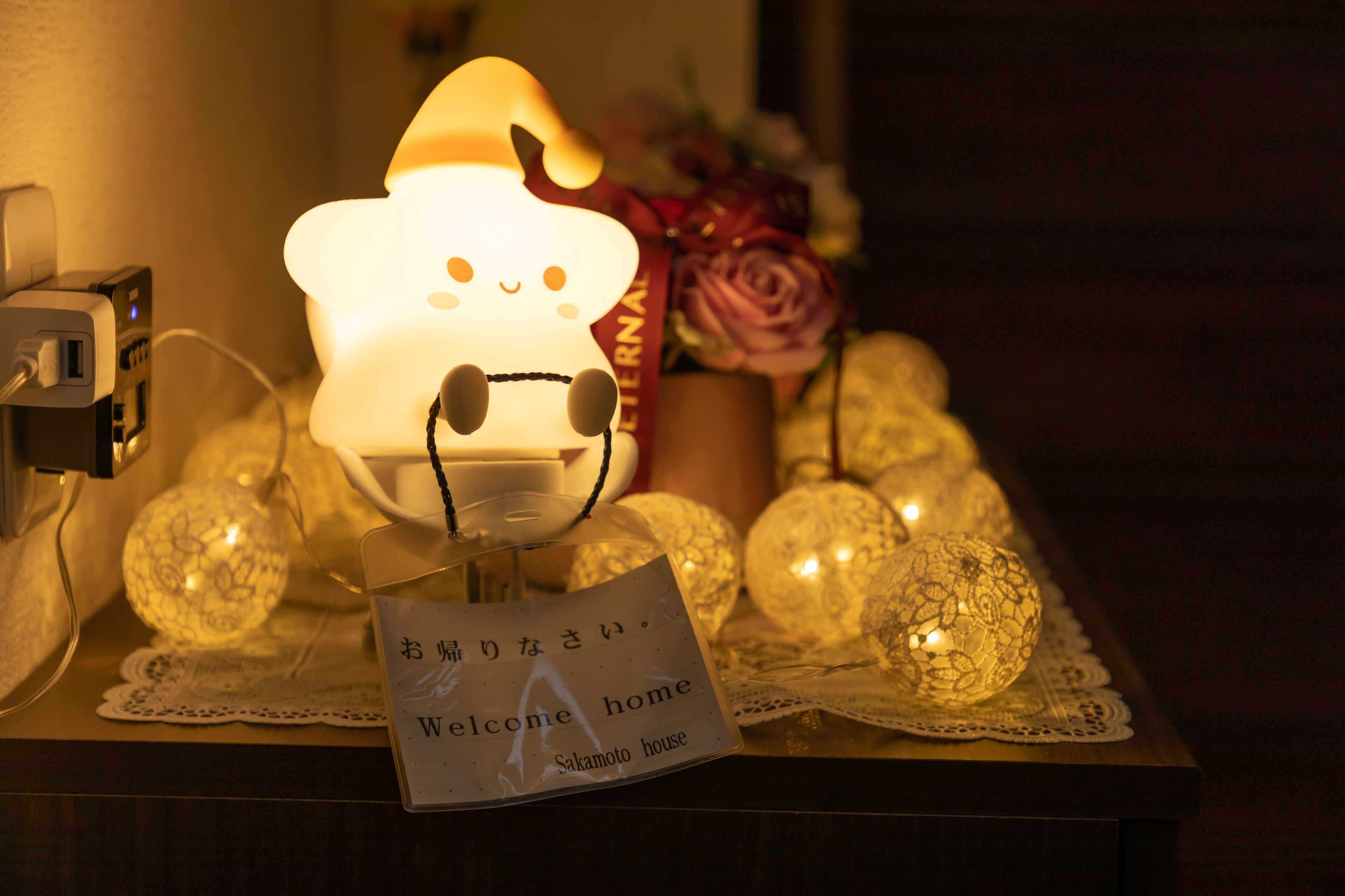 A table with a lit lamp shaped like a cat, a 'Welcome home' sign, and decorative glass spheres.
