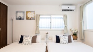 Une chambre d’hôtel avec deux lits, une fenêtre avec des rideaux, des œuvres d’art murales et un appareil de climatisation.