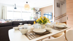 Un coin repas avec une table dressée pour quatre personnes, entouré d’un salon comprenant un canapé et un téléviseur.
