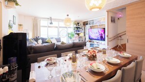 Un salon moderne avec un coin repas, un canapé, un téléviseur et une cuisine en arrière-plan.