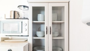 Une cuisine équipée d’un micro-ondes blanc, d’un four de la marque Hisense et d’un meuble avec des portes en verre, dans lequel sont rangées des assiettes et des bols empilés.
