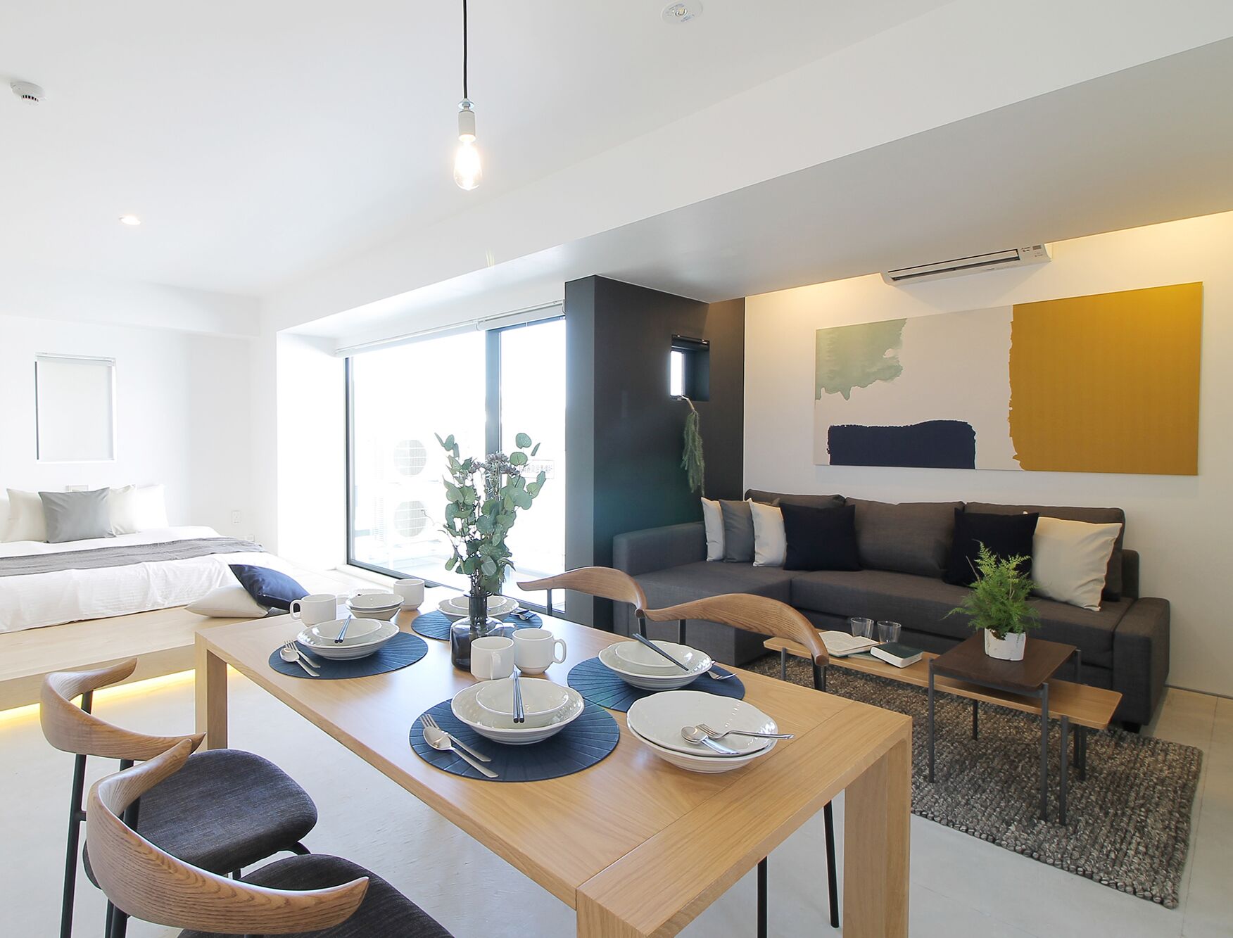 Una sala moderna con comedor, un conjunto de sofás, una mesita de centro y un amplio ventanal que proporciona luz natural.