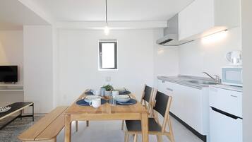 A modern kitchen with white cabinets, a built-in stove, and a microwave. There is a dining table with chairs and a bench, and a small window above the table.