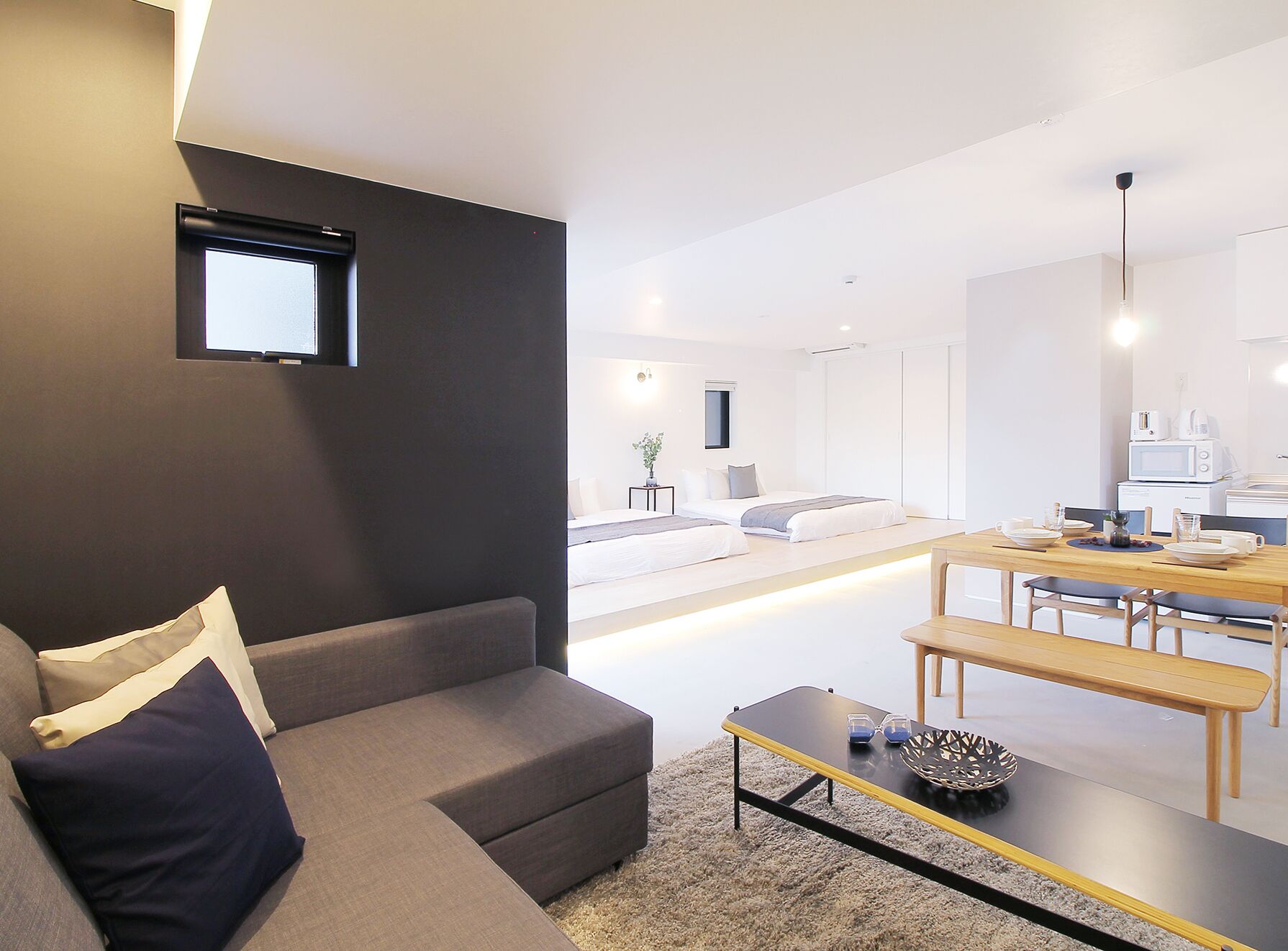 A modern living room with a grey sofa, a coffee table, and a dining area with a wooden table and chairs.