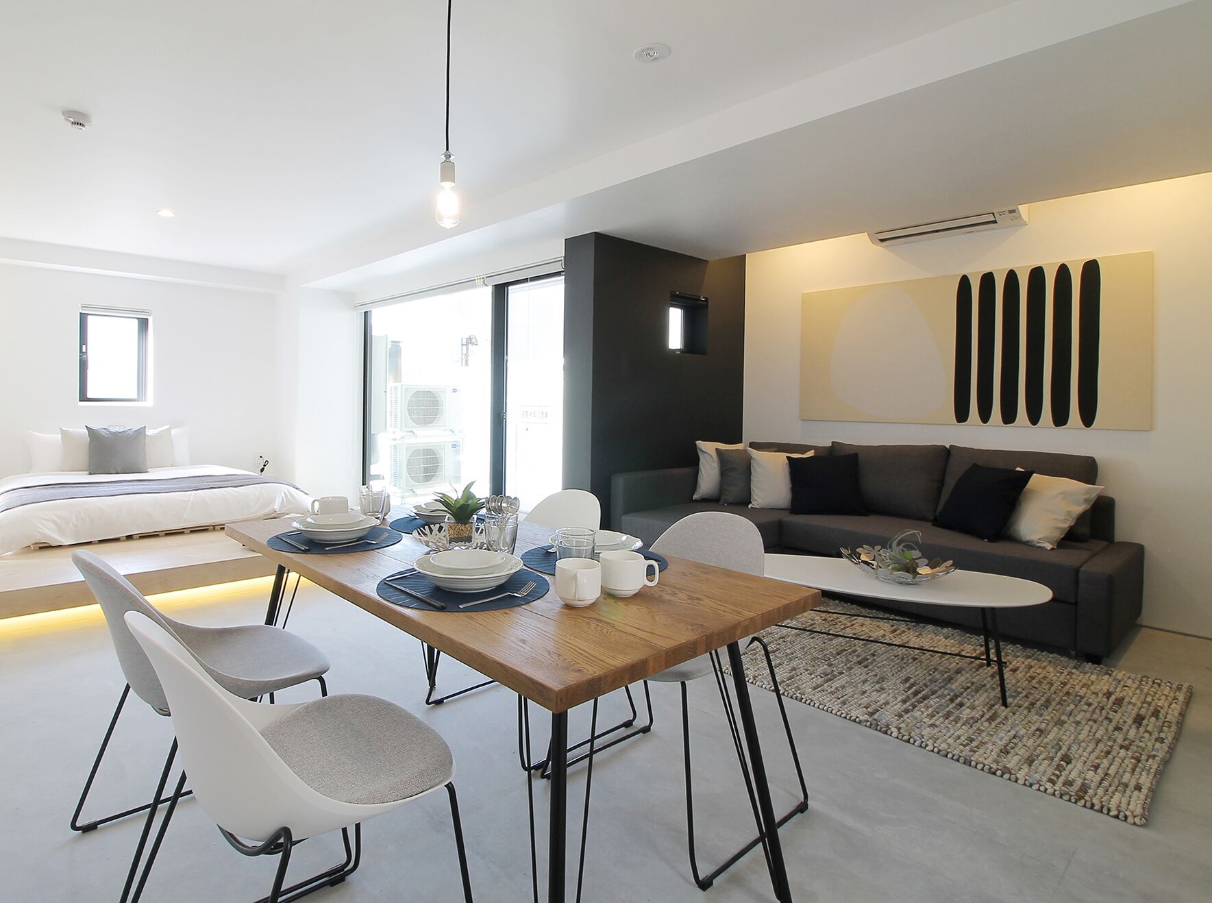 Ein modernes, helles Wohnzimmer mit Essbereich, einer Couch und einem Bett.