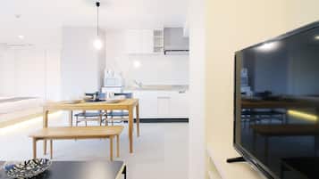 Una cocina moderna con armarios blancos, un comedor con mesas y sillas de madera, y un televisor de pantalla plana grande montado en la pared.