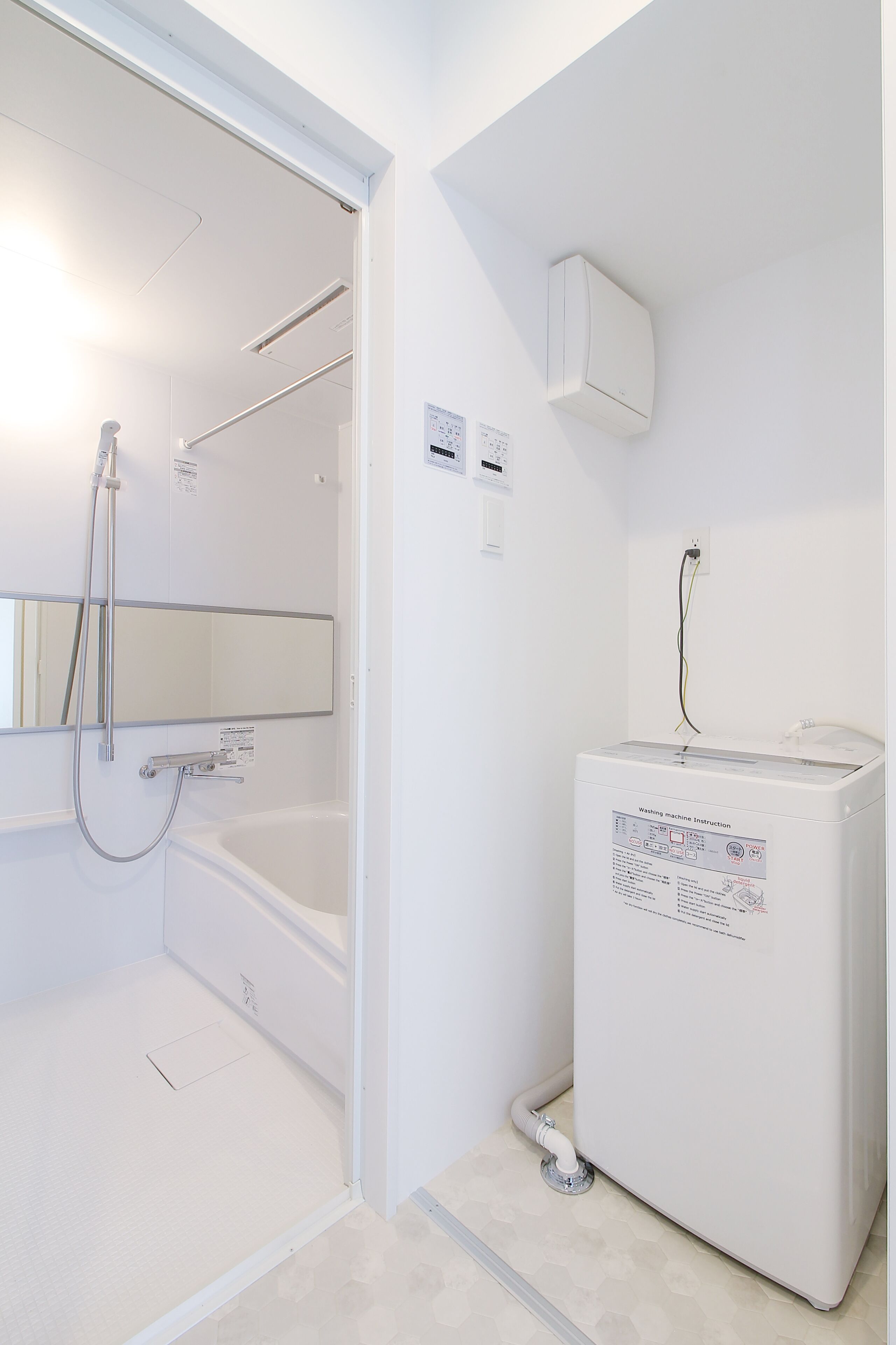 A bathroom with a white bathtub, a shower, a mirror, and a washing machine.