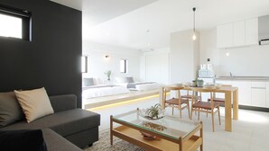 A modern living room with a sofa, a glass-top coffee table, and a dining area with wooden chairs.