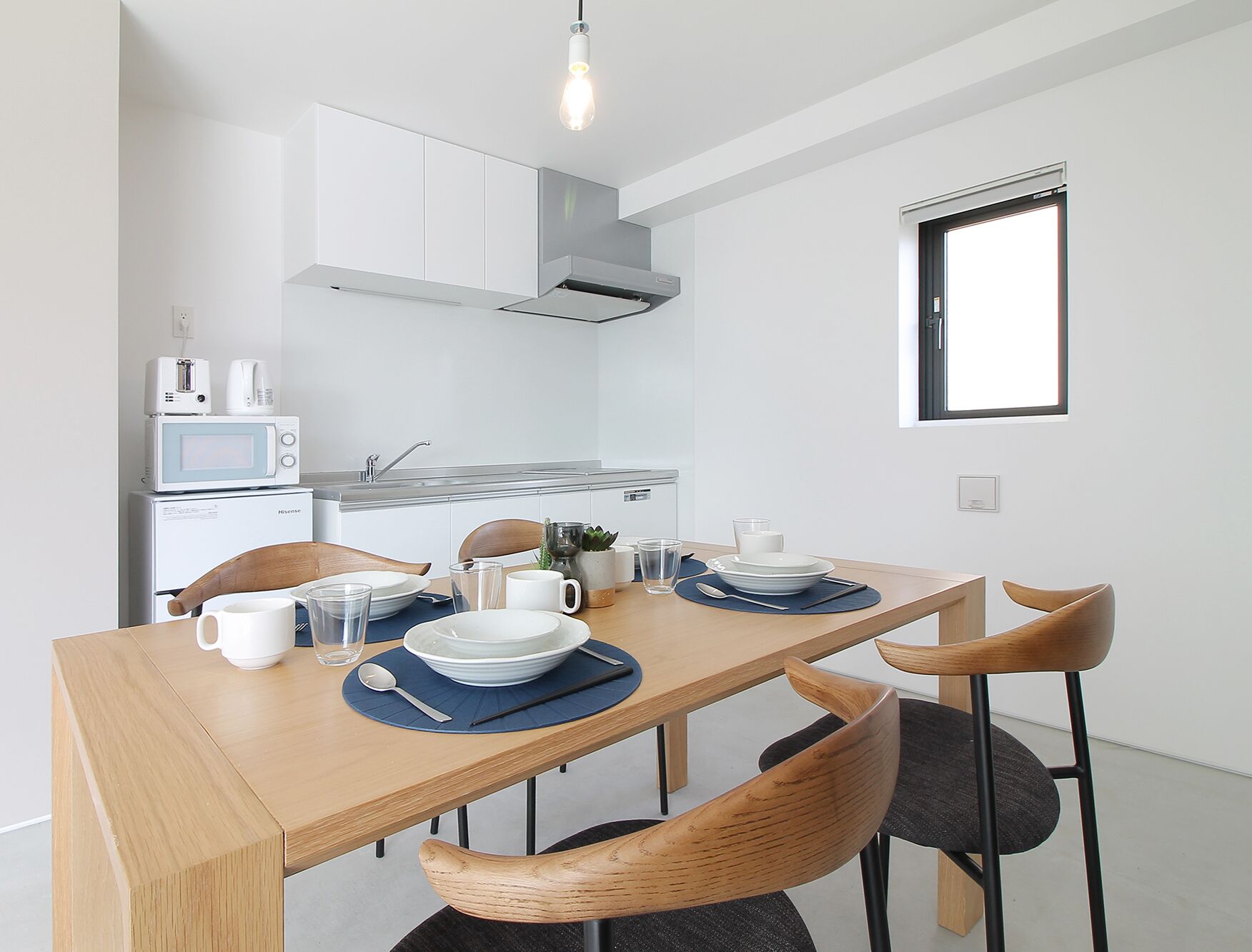 A compact kitchen with a microwave, toaster, and sink. A dining table with chairs and a window above it.