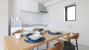 A compact kitchen with a microwave, toaster, and sink. A dining table with chairs and a window above it.