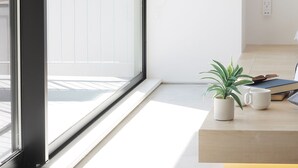 A bright room with a large window, a potted plant, a mug, and a book on a wooden table.