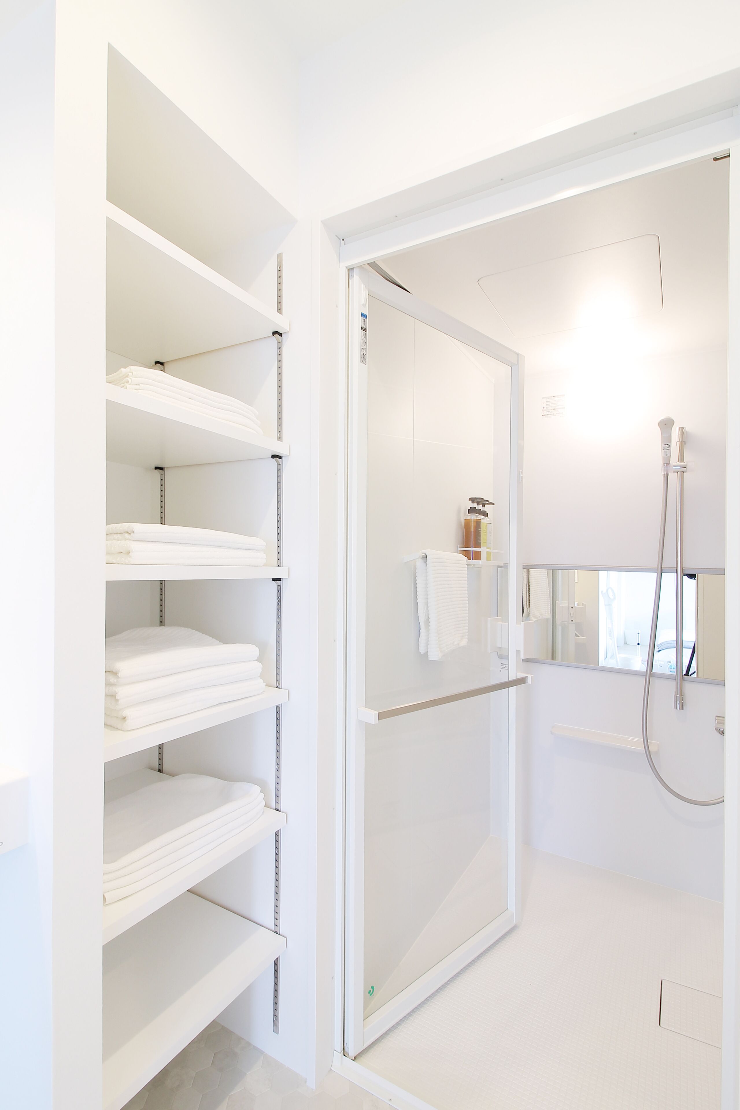 A modern bathroom with white shelves, a glass shower enclosure, and a visible towel rack.