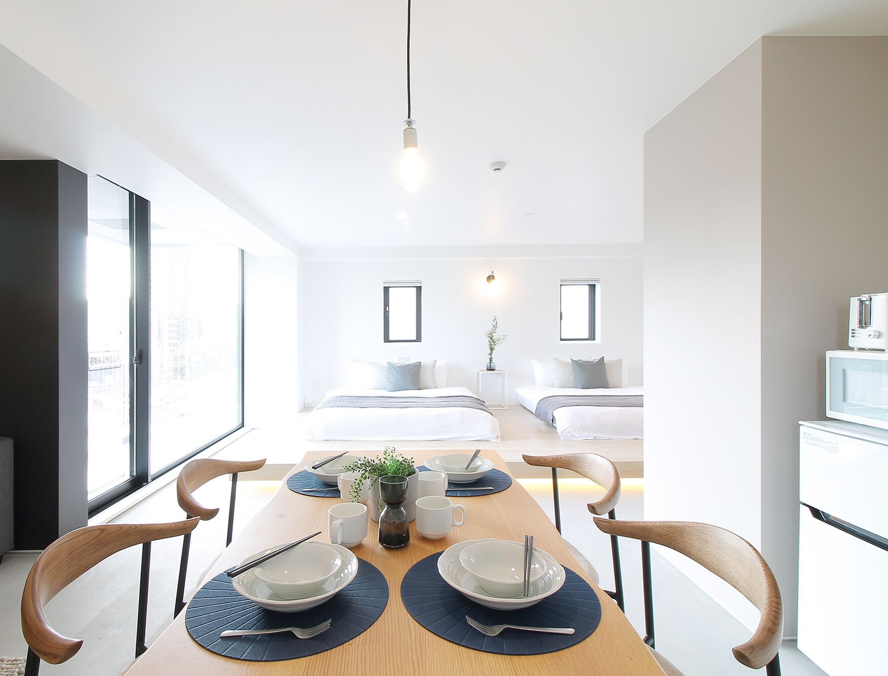 A modern, well-lit room with a dining table set for four, a bed with a view, and a small kitchen area.